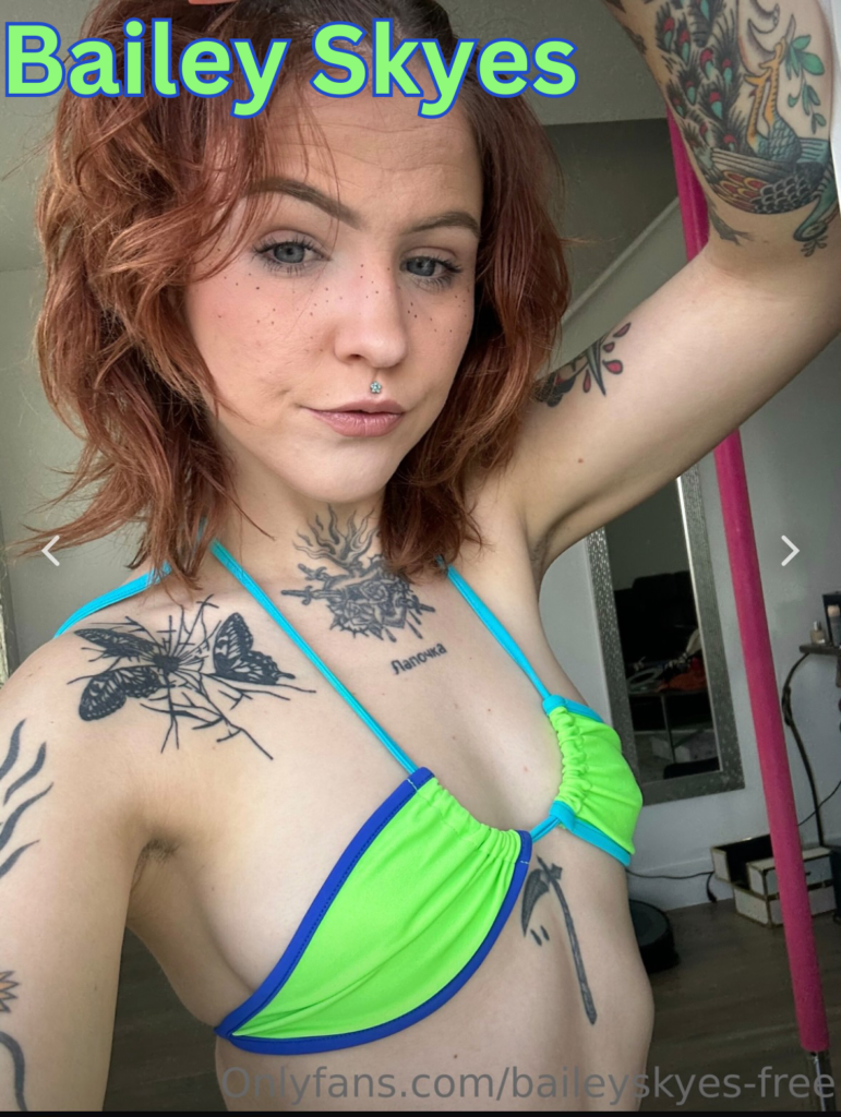 Bailey Skyes is wearing a bright green and blue-trimmed bikini top. She has red wavy hair and her pink lips are pursed.